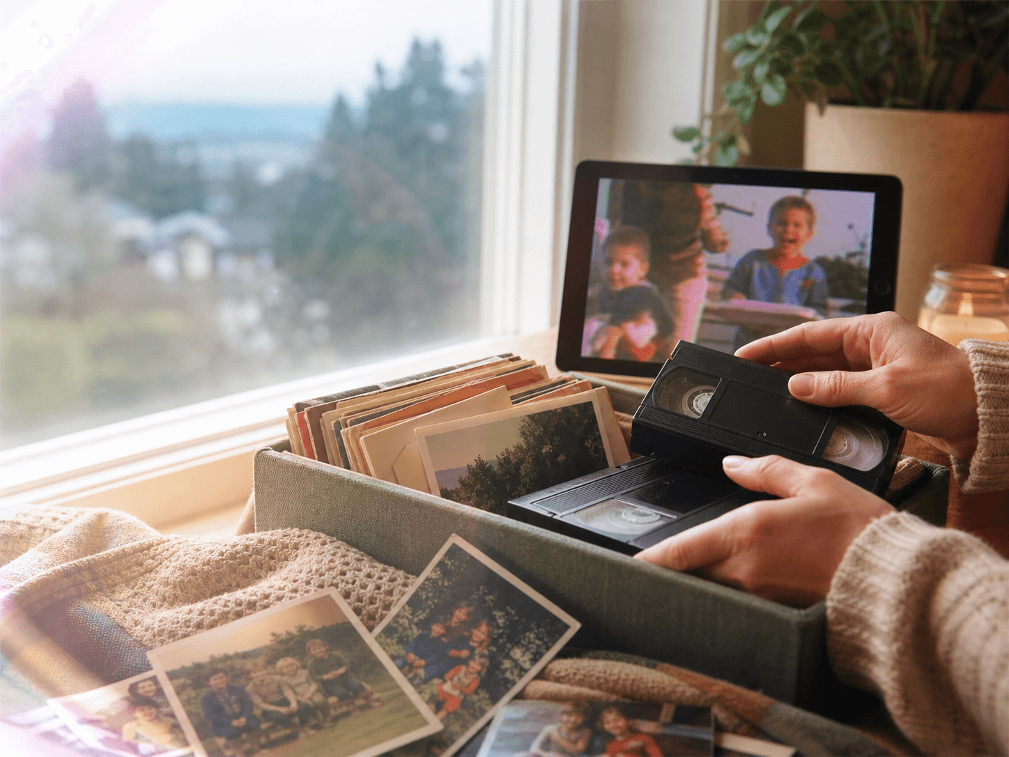 A keepsake box with old home video tapes, family photos, and a tablet showing a softened family video